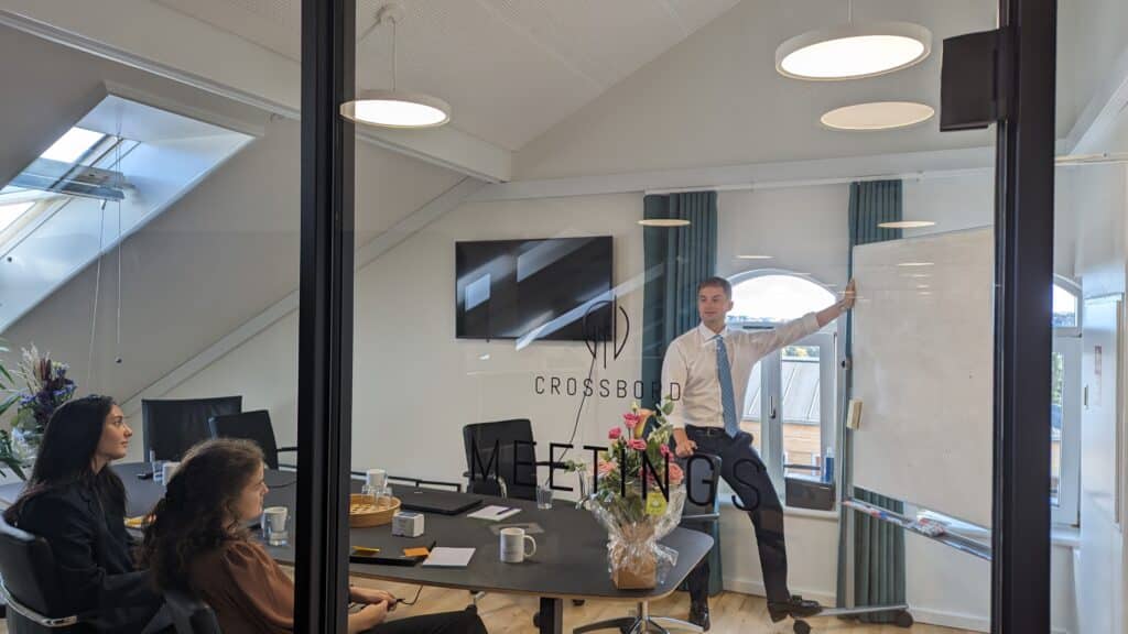 Tax consultant Mathias Kallehauge standing in front of an empty whitebord while tax trainees Dorr Hamadi and Nicoline Nielsen looks at him