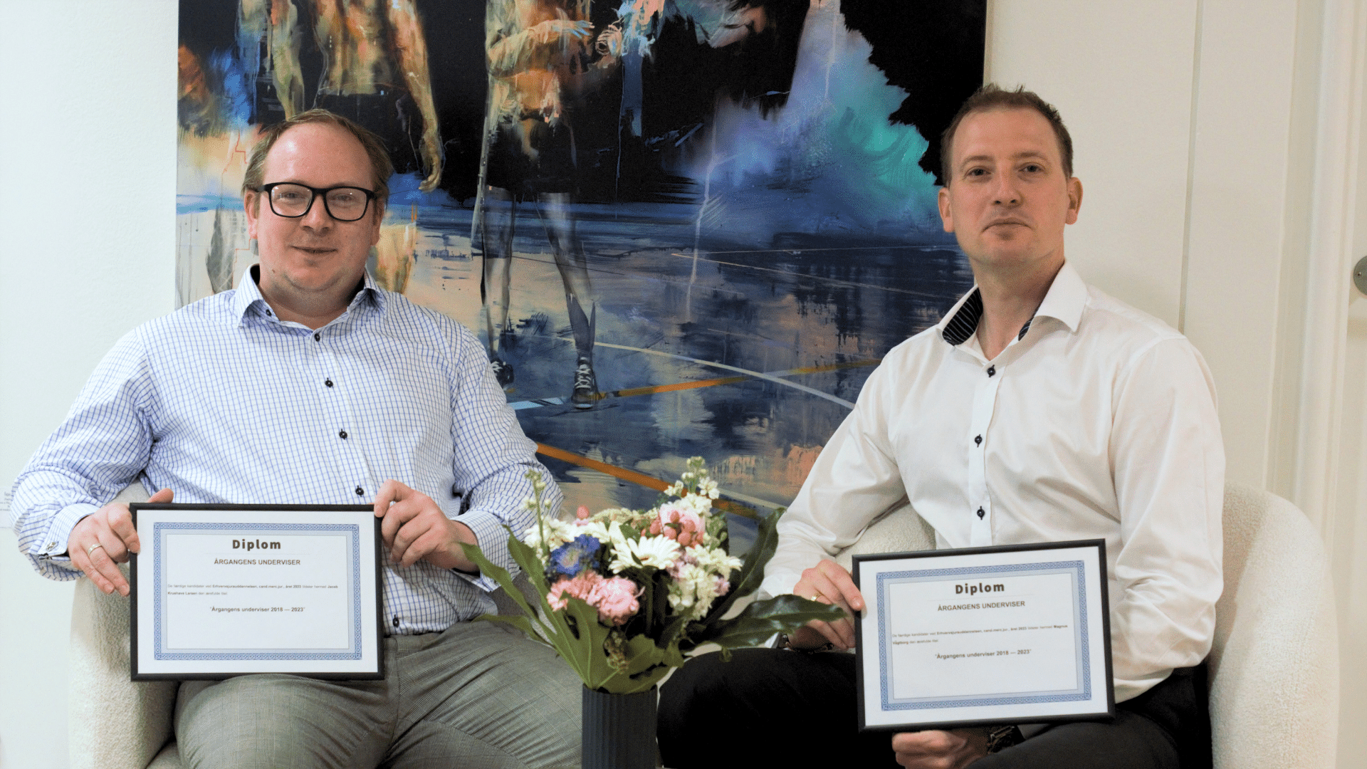 Jacob Krushave and Magnus Vagtborg Sitting in front of a Painting showing their diplomas rewarded to the Best Lecturer by the Class of 2023 Master of Science (MSc) of Business Law at Aalborg University