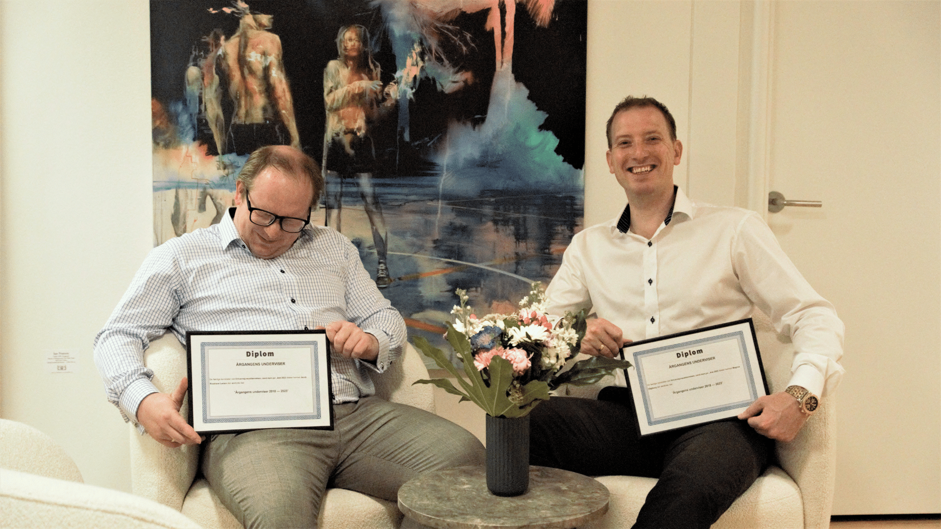 Jacob Krushave and Magnus Vagtborg Sitting in front of a Painting showing their diplomas rewarded to the Best Lecturer by the Class of 2023 Master of Science (MSc) of Business Law at Aalborg University